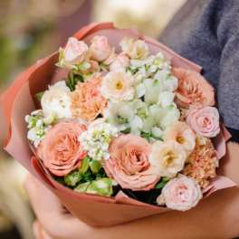 Handheld bouquet of peach, pink, and white flowers wrapped in pink paper