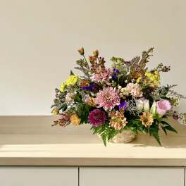 Mixed bouquet in a woven basket with pink, yellow, and purple flowers