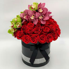 Red roses and pink orchids arranged in a black hat box with a ribbon.
