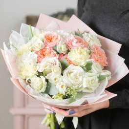 Handheld bouquet of white and peach flowers wrapped in pink paper