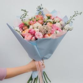 Handheld bouquet of pink and peach roses wrapped in pale blue paper
