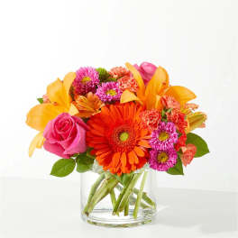 Bright mixed bouquet in a clear glass vase with orange, pink, and purple flowers.
