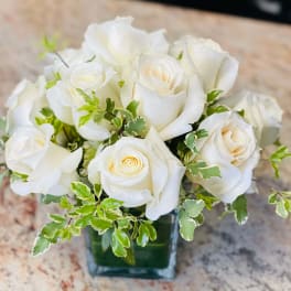 White rose bouquet in a square glass vase with variegated greenery