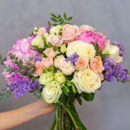 Handheld bouquet of pastel roses and purple filler flowers