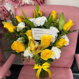 Yellow roses and white carnations in a glass vase with a butterfly decoration.