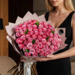 Woman holding a large bouquet of pink roses wrapped in pale paper
