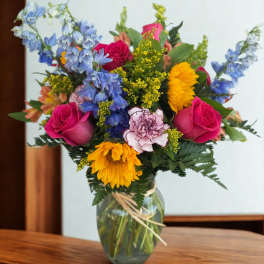 Mixed bouquet of roses, sunflowers, and blue flowers in a glass vase