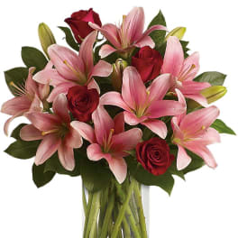 Pink lilies and red roses arranged in a clear glass vase