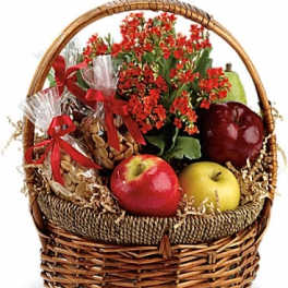 Gift basket with red flowers, apples, and wrapped snacks in a wicker basket