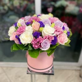 Round bouquet of pink, white, and lavender roses in a pink hat box