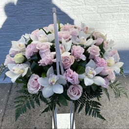 Basket arrangement of pale pink roses and white orchids on a stand