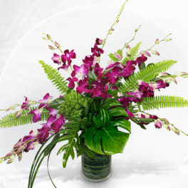 Purple orchid arrangement in a glass vase with tropical foliage