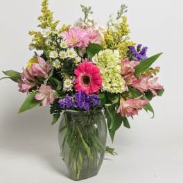 Mixed bouquet of pink gerbera, daisies, alstroemeria, and hydrangea in a clear glass vase