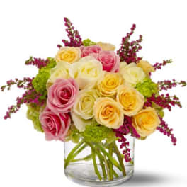 Low arrangement of pastel roses with green accents in a clear glass vase