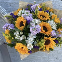 Bouquet of sunflowers, white alstroemeria, and lavender flowers in newspaper wrap