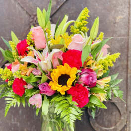 Mixed bouquet of roses, lilies, sunflowers, and carnations in a glass vase