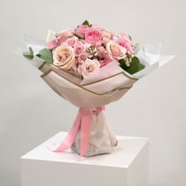 Pink and blush rose bouquet wrapped in pale paper with a pink ribbon