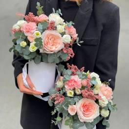 Two pastel flower arrangements in white hat boxes held by a person