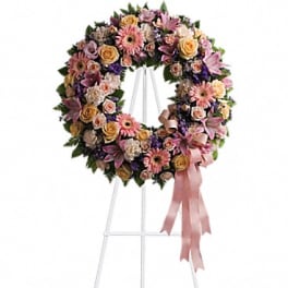 Heart-shaped floral wreath on a stand with pink and peach flowers and ribbon
