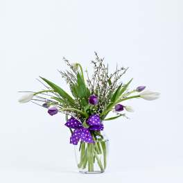 Purple and white tulips in a clear glass vase with a polka-dot ribbon