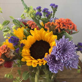 Mixed bouquet with a sunflower, purple chrysanthemums, and orange cockscomb in a glass vase
