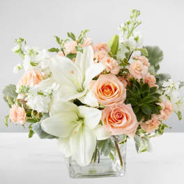 Peach roses and white lilies in a clear glass vase