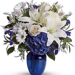 White lilies and daisies arranged in a blue vase with purple accents