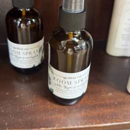Two amber room spray bottles with clear caps sit on a wooden shelf.