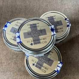 Four small tins of muscle rescue balm on a wooden surface