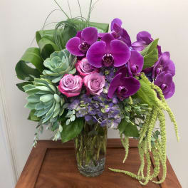 Purple orchids and pink roses in a clear glass vase