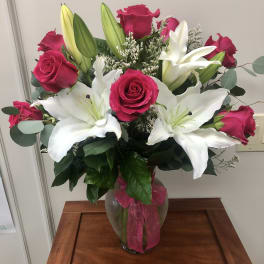 Arrangement of hot pink roses and white lilies in a clear glass vase with a pink ribbon bow