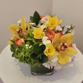 Yellow orchids and roses arranged in a square glass vase