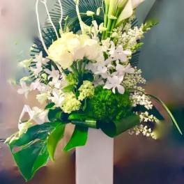 White floral arrangement with calla lilies and orchids in a tall vase