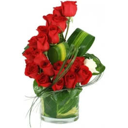 Red roses arranged in a clear glass vase with green leaves