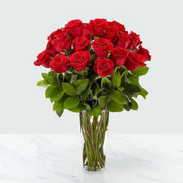 Tall clear glass vase filled with a large bouquet of long-stemmed red roses.