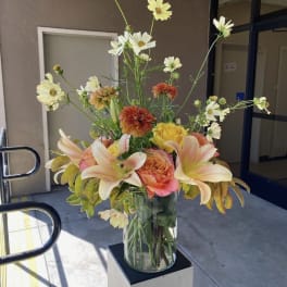 Tall mixed bouquet in a clear glass vase with lilies, roses, and daisies