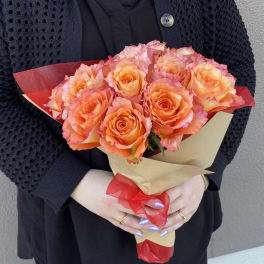 Bouquet of orange and pink roses wrapped in tan paper with red ribbon
