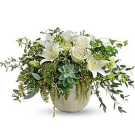 White lilies and roses in a low ceramic vase with trailing greenery