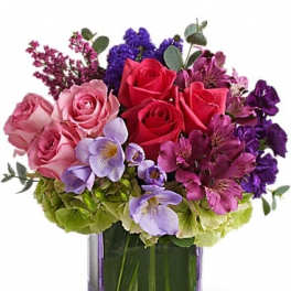Mixed bouquet of roses, hydrangeas, and purple flowers in a square glass vase