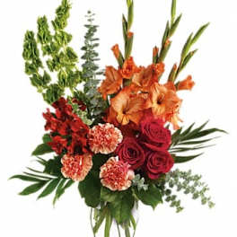 Tall bouquet of orange gladiolus, red roses, and carnations in a clear vase