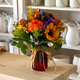 Bouquet of sunflowers, roses, and purple flowers in a red glass vase