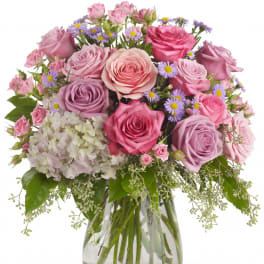 Pink and lavender roses with hydrangea and asters arranged in a clear glass vase