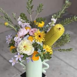 Mixed bouquet in a mint vase with yellow, pink, and lavender blooms