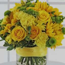 Yellow roses and sunflowers arranged in a glass vase with a yellow ribbon.