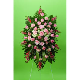 Standing floral spray of pink roses and carnations on a green backdrop