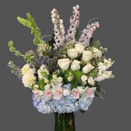 Tall bouquet of white roses, blue hydrangeas, and pale orchids in a glass vase