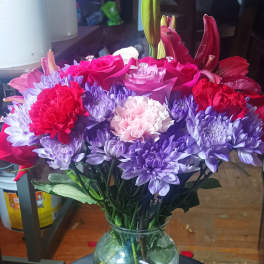 Mixed bouquet of pink roses, purple chrysanthemums, and red carnations in a glass vase