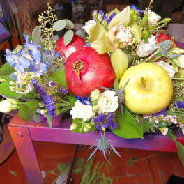 Mixed floral arrangement with pomegranates and apples on a purple table