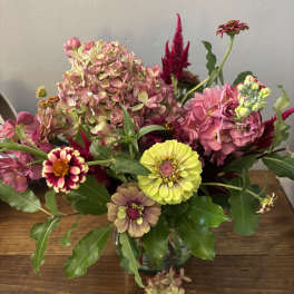 Mixed bouquet with pink hydrangeas, zinnias, and yellow blooms in a glass vase