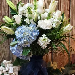 Large bouquet of white lilies, white blooms, and blue hydrangeas in a dark vase
